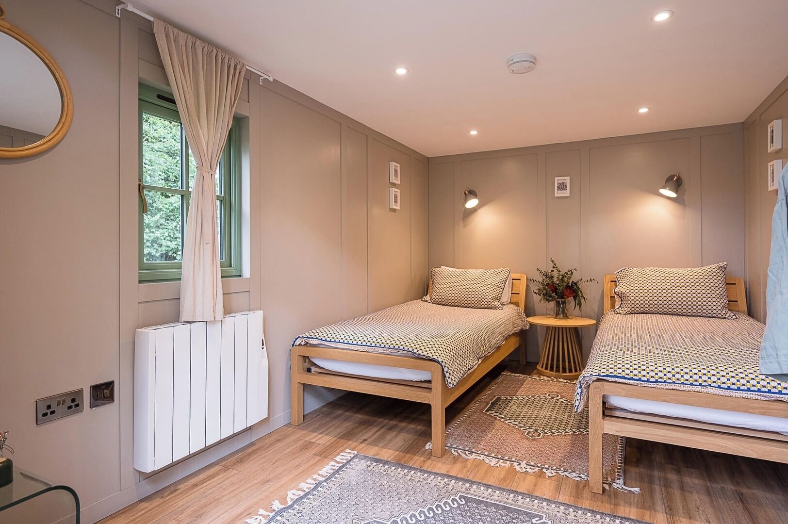 Une chambre avec deux lits, un radiateur, une petite table avec un vase et une fenêtre avec des rideaux.