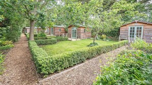 A wooden cabin-style hotel with a well-maintained garden, a gravel path, and a clear view of the surrounding trees. - Feather Lodge, Toad Hall, Wangford (Wangford)