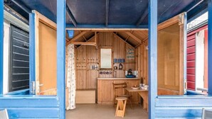 A compact kitchen with wooden cabinets, a small table, and a chair. - Driftwood Beach Hut, Southwold (Suffolk)