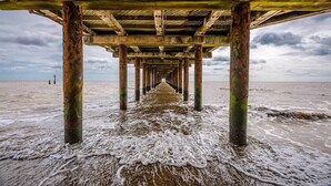 A pier extending into the sea with a wooden structure and concrete pillars.