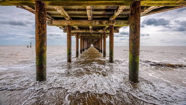 A pier extending into the sea with a wooden structure and concrete pillars. - Driftwood Beach Hut, Southwold (Suffolk)
