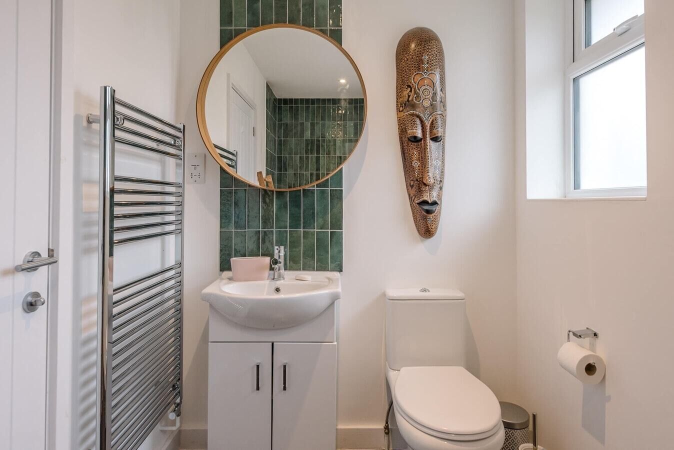 A bathroom with a white sink, a toilet, a mirror, and a decorative mask on the wall.