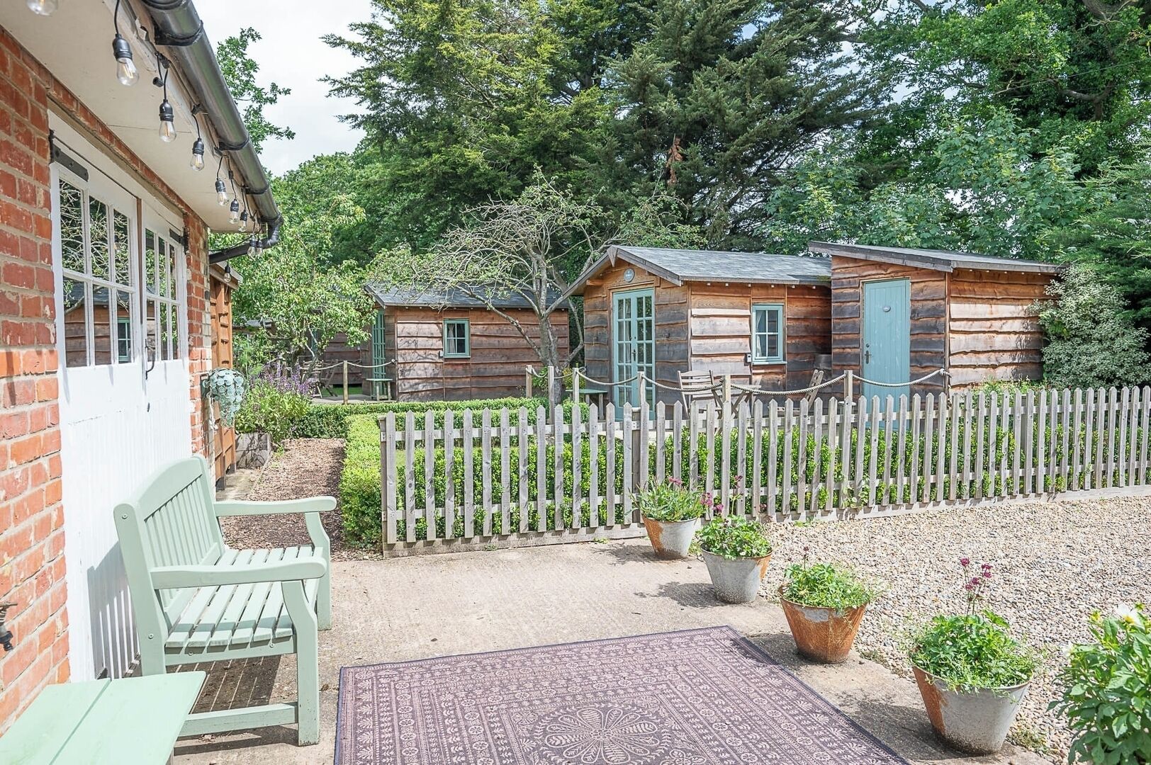 A rustic cabin with a wooden fence, a bench, and potted plants.