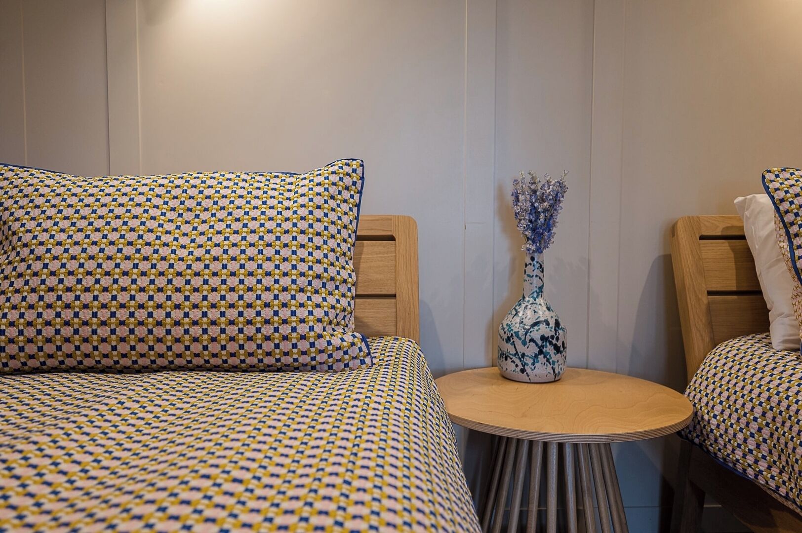 A room with a bed, two chairs, a small round table, and a vase with flowers.