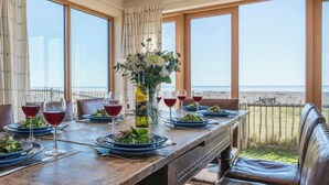 A dining table set with plates, glasses, and a bottle of wine, overlooking a beach. - Fairhaven, Thorpeness (Thorpeness)