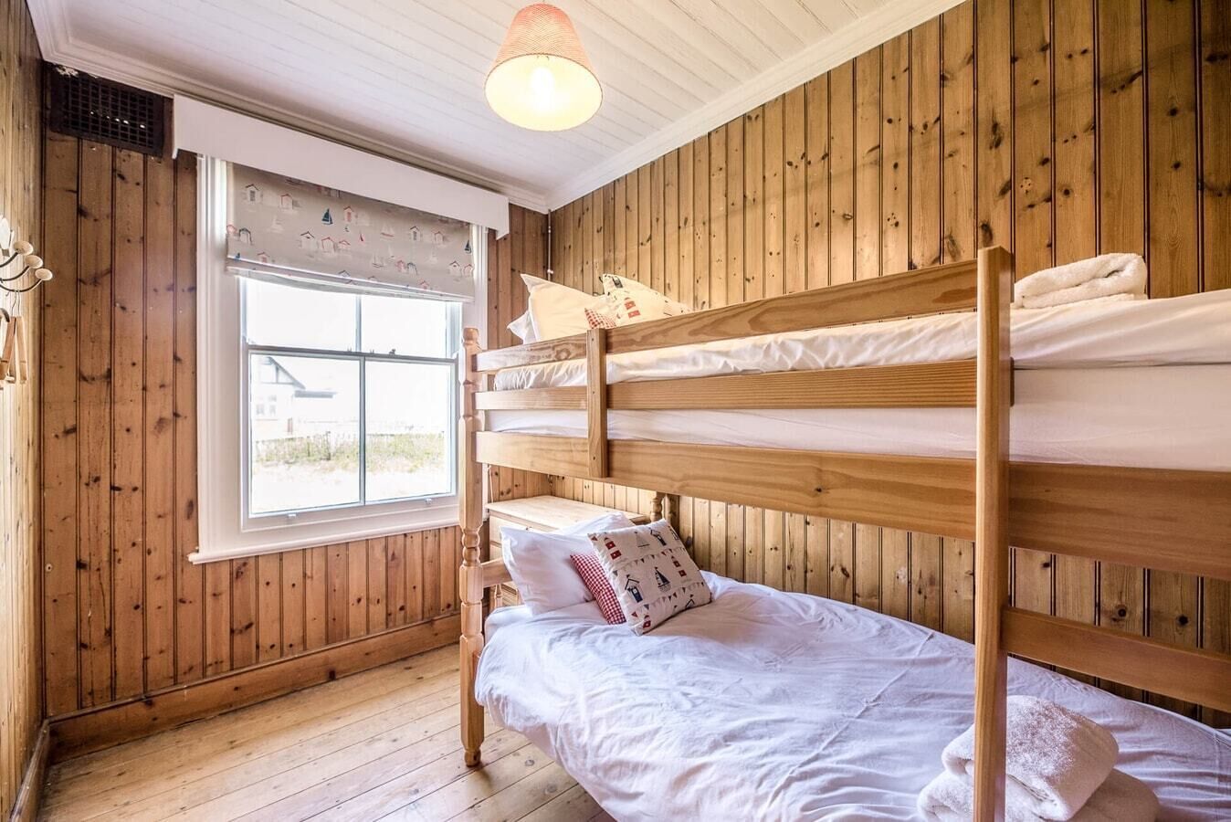 Een slaapkamer met stapelbedden, houten wanden en een raam met uitzicht op huizen.