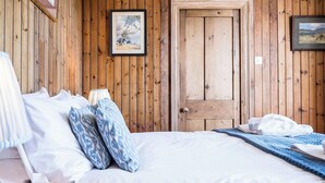 A wooden-paneled room with a bed, pillows, a lamp, and a door. - Fairhaven, Thorpeness (Thorpeness)