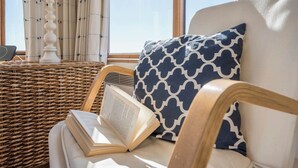 A wicker chair with a book and a pillow, a white sofa, and a window with curtains. - Fairhaven, Thorpeness (Thorpeness)