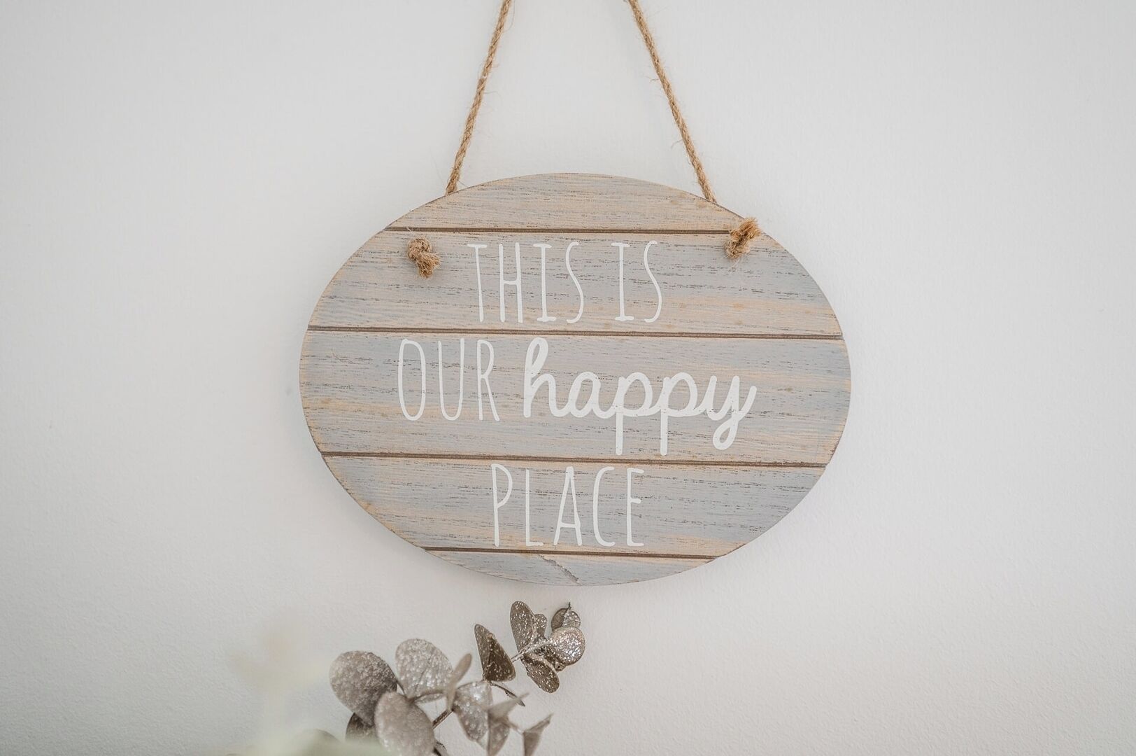 Un letrero de madera circular con el texto 'THIS IS OUR happy PLACE' colgado en una pared.