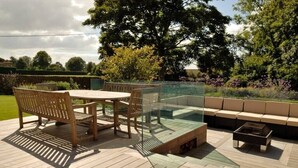 An outdoor deck with a glass enclosure, wooden furniture, and a fire pit.