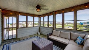 A sunroom with large windows, a ceiling fan, and a wicker ottoman. - 5813- Crowe's Nest, South Nags Head with Private Pool, Pool Table and Ocean View...Family Fun! (Nags Head)