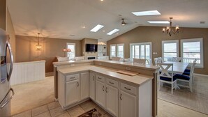 A spacious kitchen with a large island, white cabinetry, and a dining area with blue chairs. - 5813- Crowe's Nest, South Nags Head with Private Pool, Pool Table and Ocean View...Family Fun! (Nags Head)