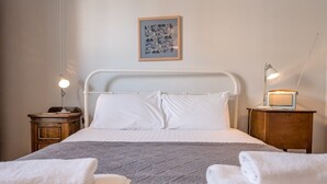 A neatly made bed with white linens, a gray blanket, and two rolled towels on the side. There is a framed picture on the wall above the bed.