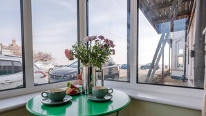 A small table with two green cups and saucers, a vase with flowers, and a plate with strawberries.