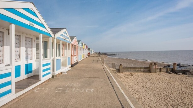 A row of beach huts with a sandy path leading to the beach.