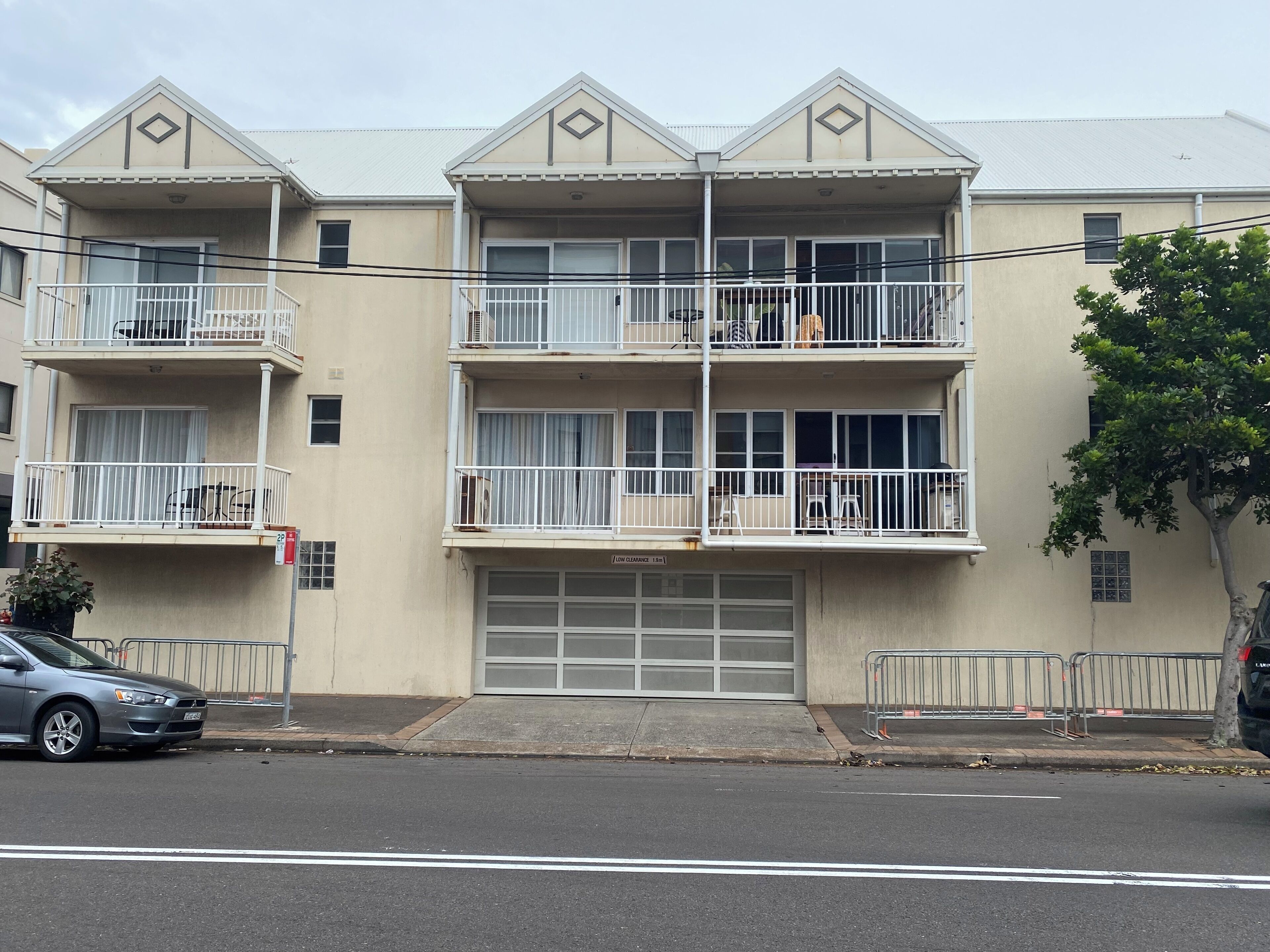 A multi-story residential building with balconies, a garage, and a street view.