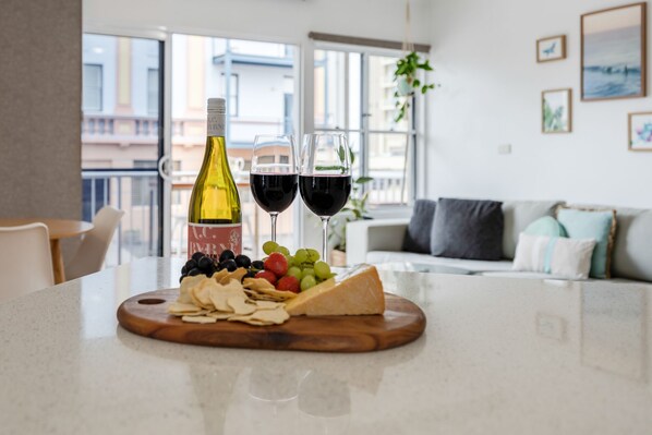 A dining table with a bottle of wine, two glasses of red wine, a variety of cheeses, and fruits.