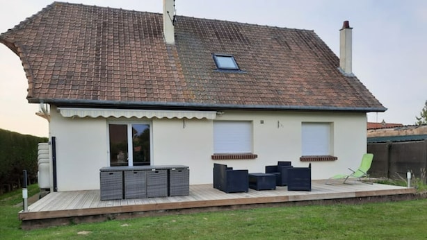 Ein Haus mit Ziegeldach, einer überdachten Terrasse mit Gartenmöbeln und einem Rasen.