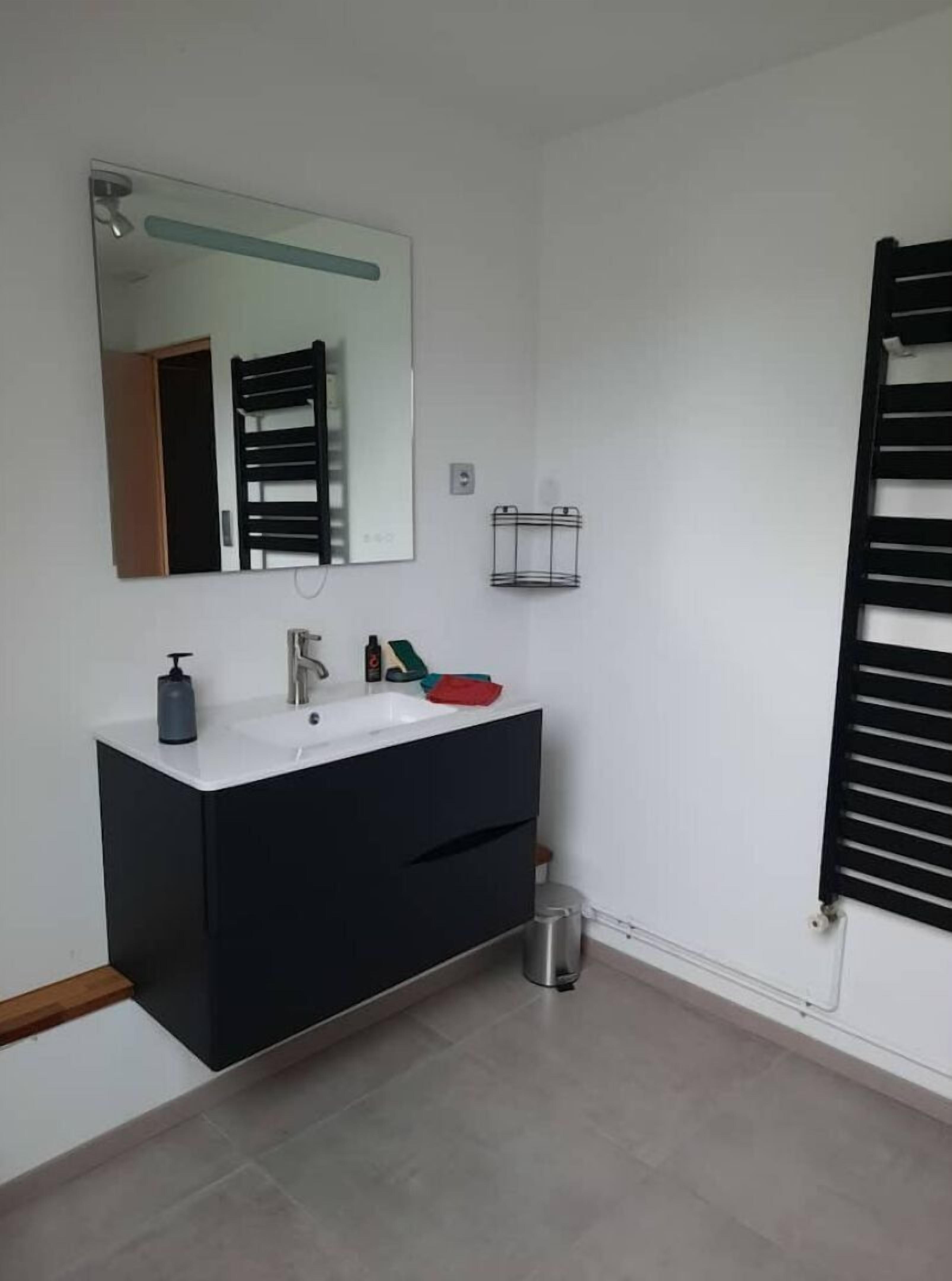 Une salle de bain moderne avec un meuble-lavabo blanc, un grand miroir, un porte-serviettes et une petite poubelle.