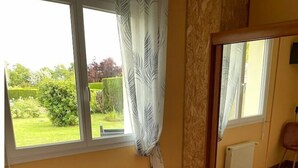 Ein Schlafzimmer mit Bett, Heizkörper, einem Fenster mit Vorhängen und Blick auf einen Garten.