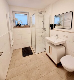 A modern bathroom with a glass shower enclosure, a white sink, and a toilet. - Modern basement apartment in the Munich district (Bruck)
