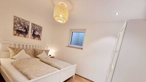 A bedroom with a bed, a nightstand, a window, and two wall art pieces. - Basement Apartment in the Munich/Ebersberg District—Affordable during the winter months—minimum stay of 7 days (Bruck)