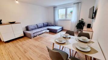A modern living room with a dining area, a sofa, a TV, and a window with curtains.