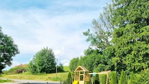 A fenced playground with a slide and swing set, surrounded by green grass and trees. - Basement Apartment in the Munich/Ebersberg District—Affordable during the winter months—minimum stay of 7 days (Bruck)