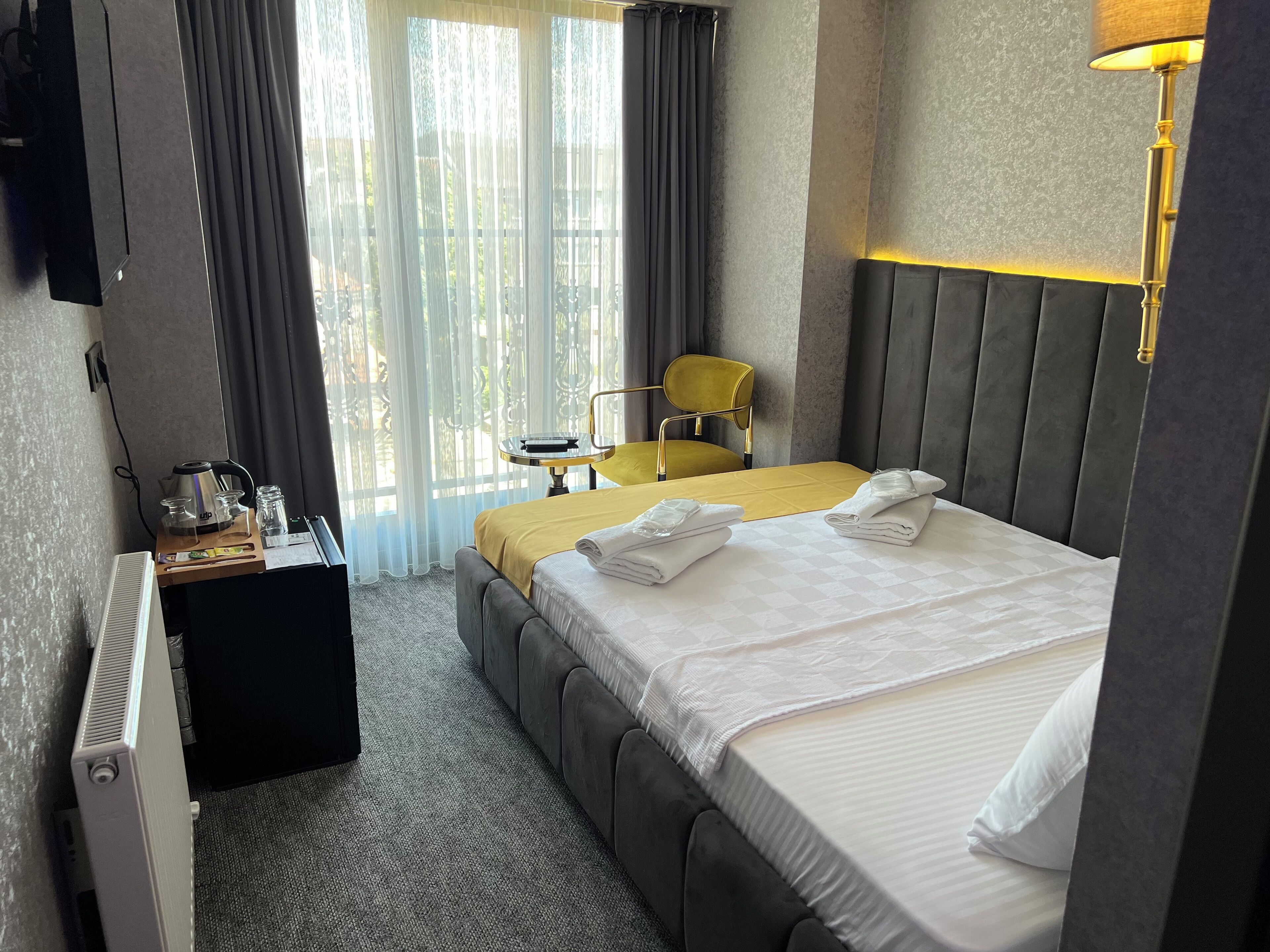 Una camera d'albergo con un letto, una scrivania con un bollitore, una sedia e una lampada.