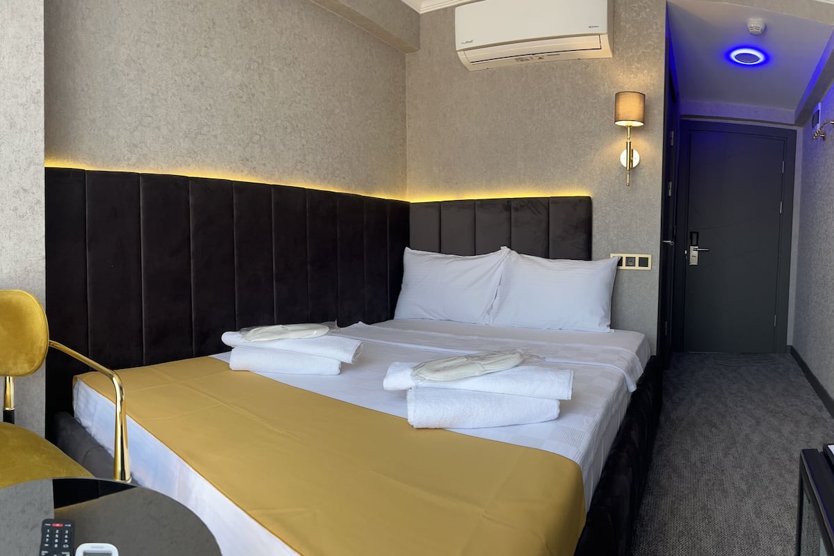 A hotel room with a bed, a desk, a chair, a lamp, and a TV.
