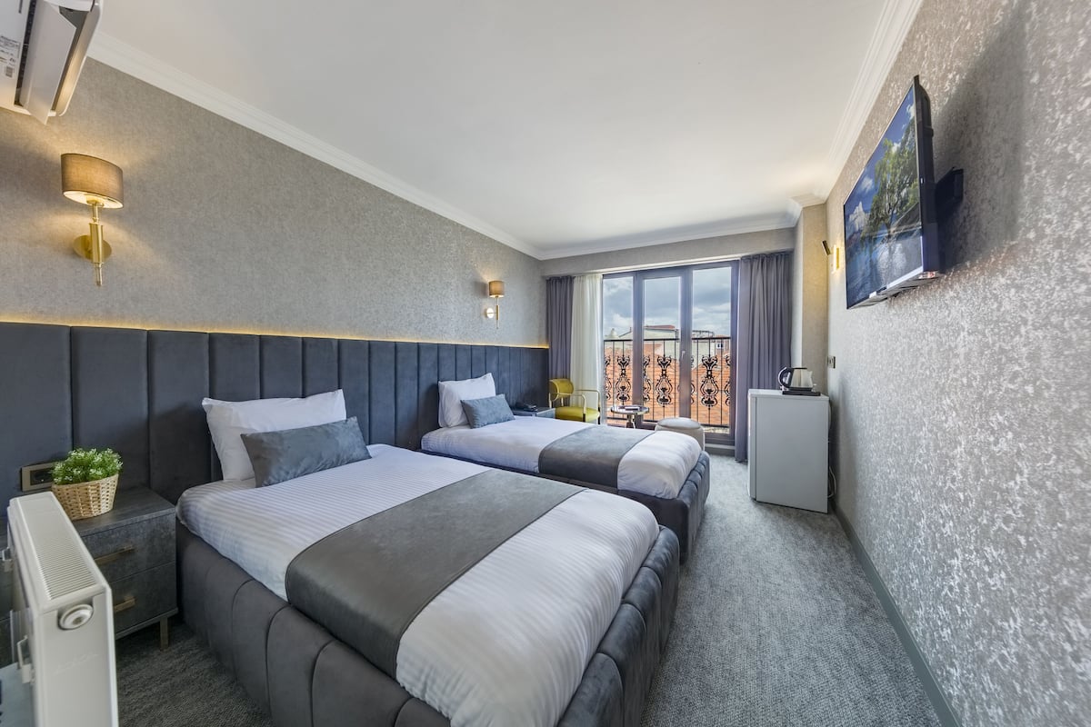 A hotel room with two beds, a TV mounted on the wall, a small table, and a view of the city.