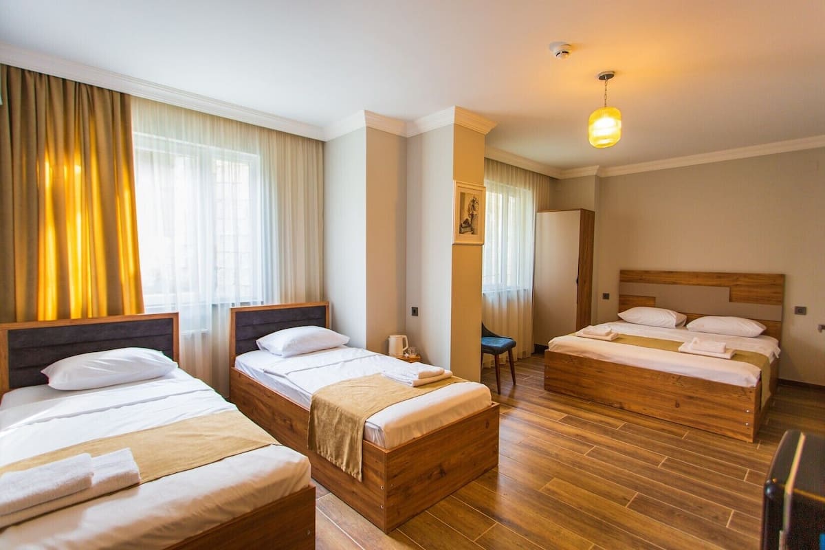 A hotel room with three wooden beds, a wooden floor, and a large window with curtains.