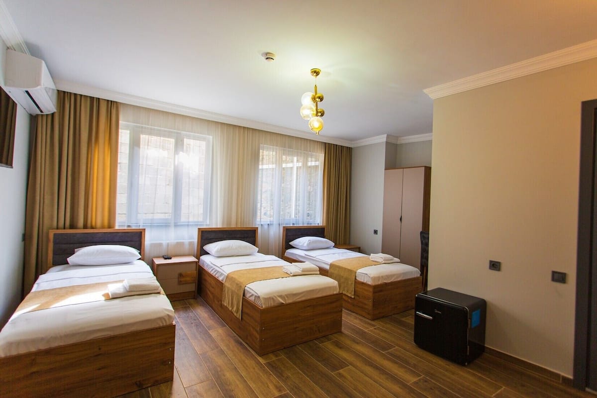 A hotel room with three wooden beds, a wardrobe, a desk, and a small black speaker.