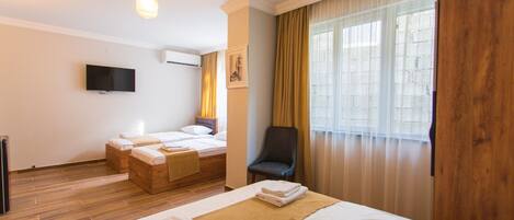 A hotel room with two beds, a TV, a chair, and a window with curtains.