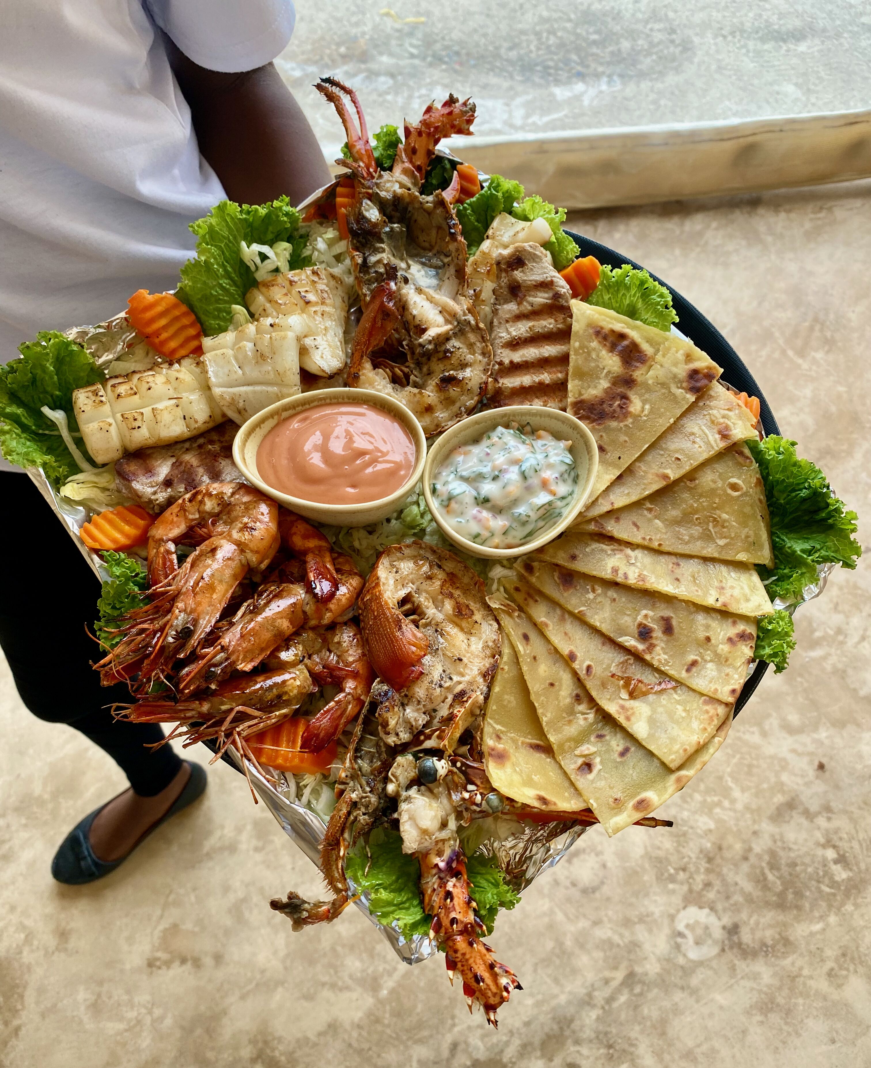Una bandeja con mariscos a la parrilla, pan plano y dos salsas para mojar.