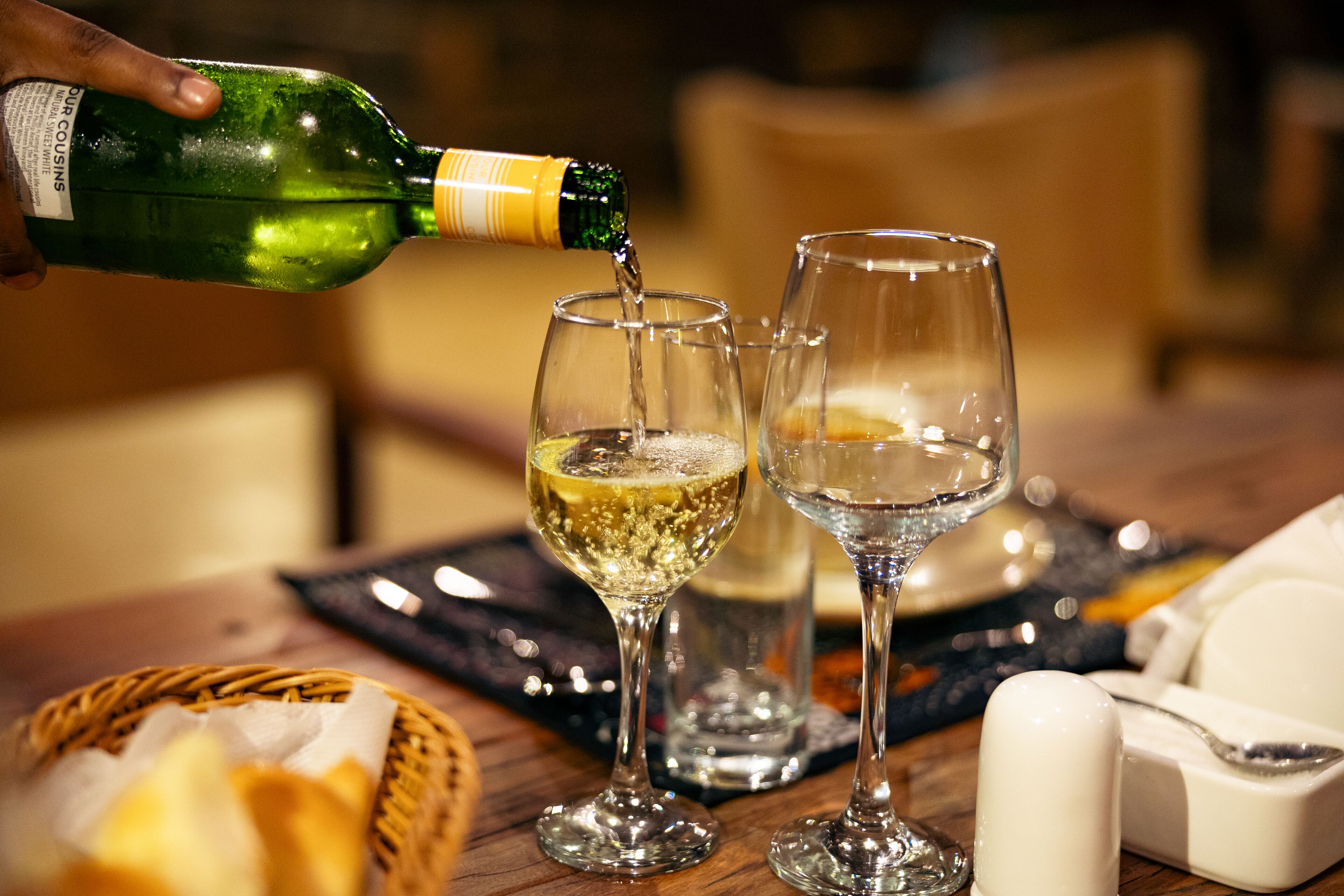 A bottle of champagne being poured into two glasses on a wooden table.