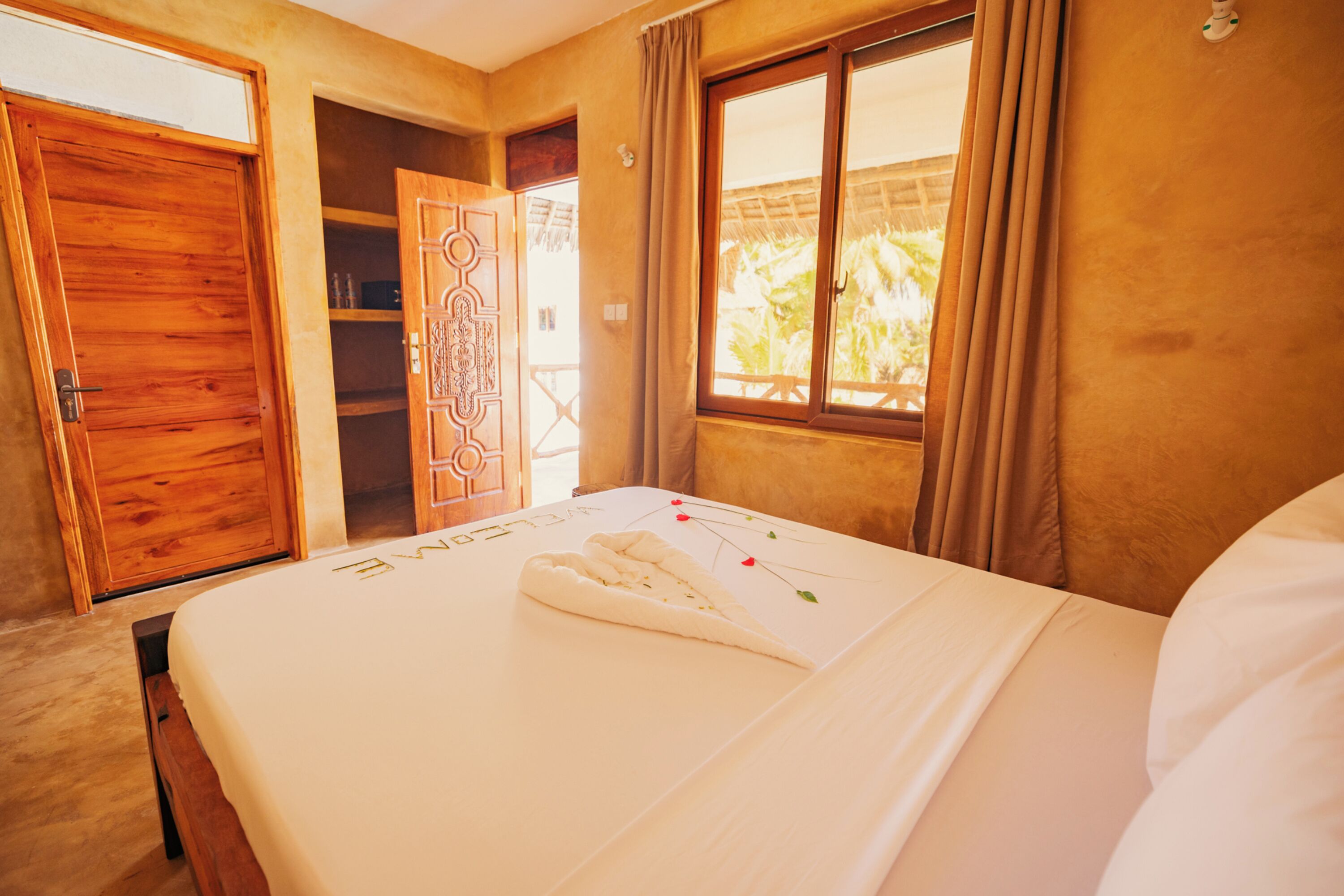 A bedroom with a wooden door, a window with curtains, and a bed with a towel and a decorative item on it.