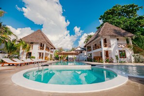 A pool area with lounge chairs and two buildings with thatched roofs. - Mayai Ocean Resort (Bwejuu)