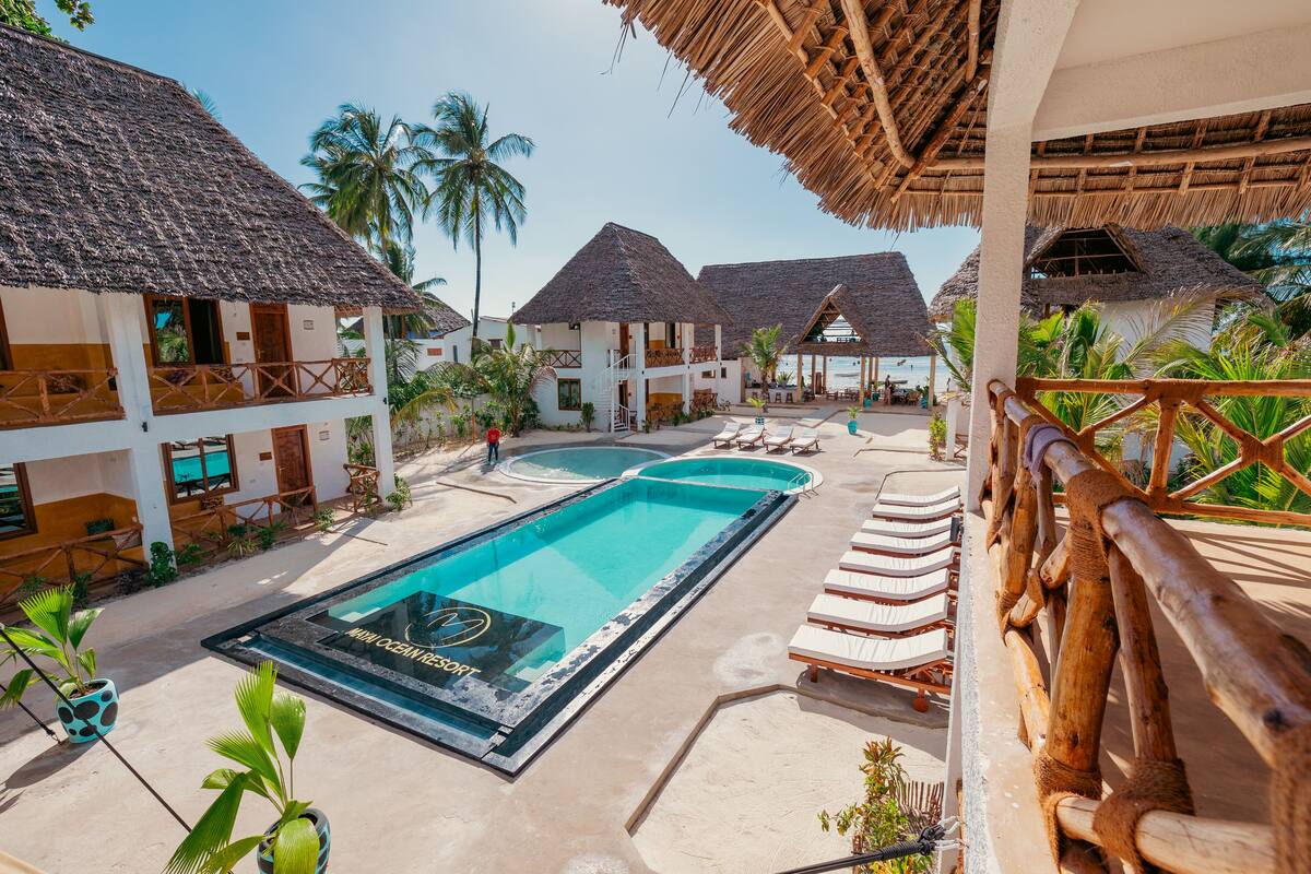 Un resort con piscina central, edificios con techo de paja y zonas de descanso con tumbonas.