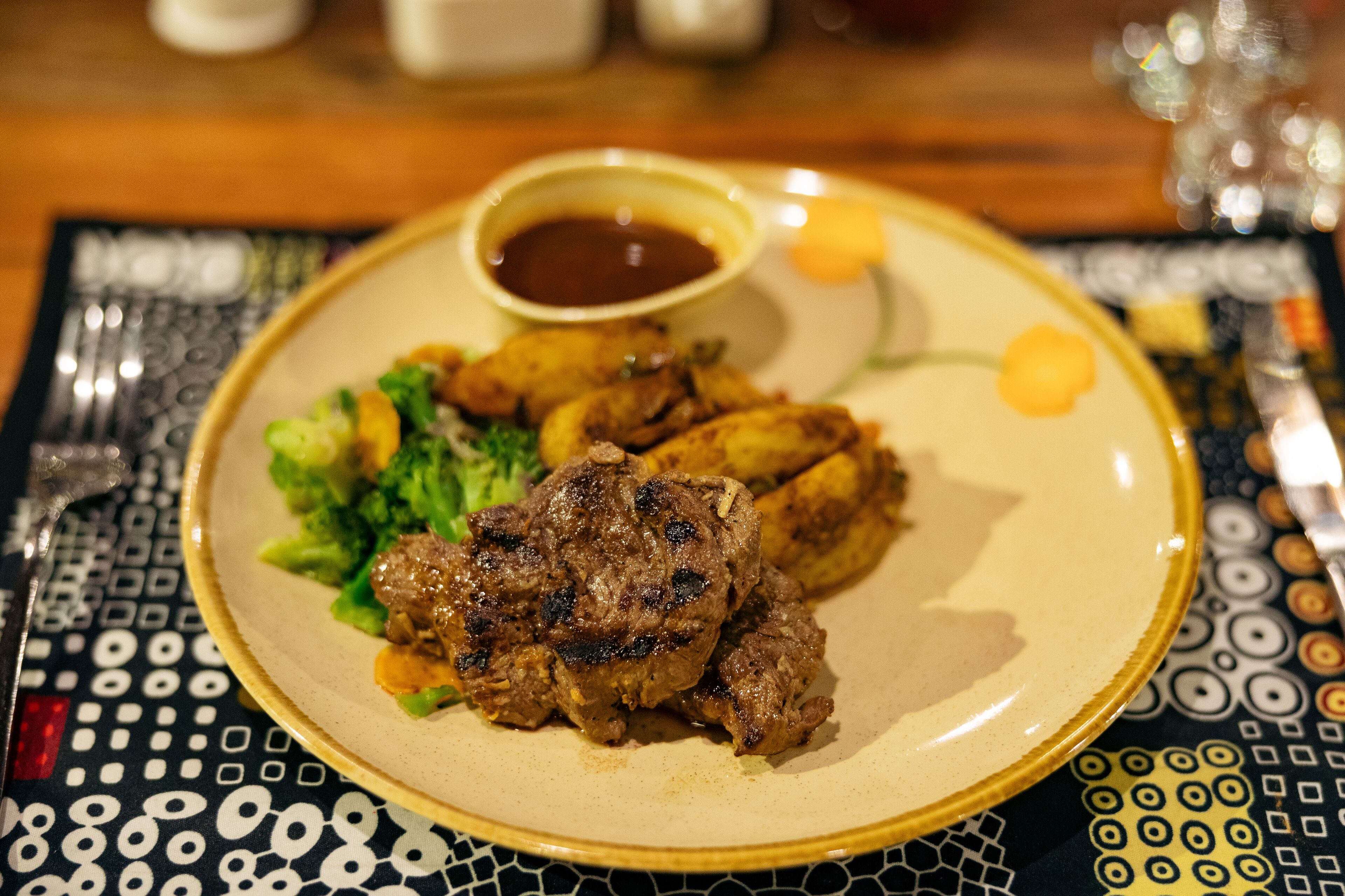 A plate with grilled meat, potatoes, and a side salad, accompanied by a small bowl of sauce.