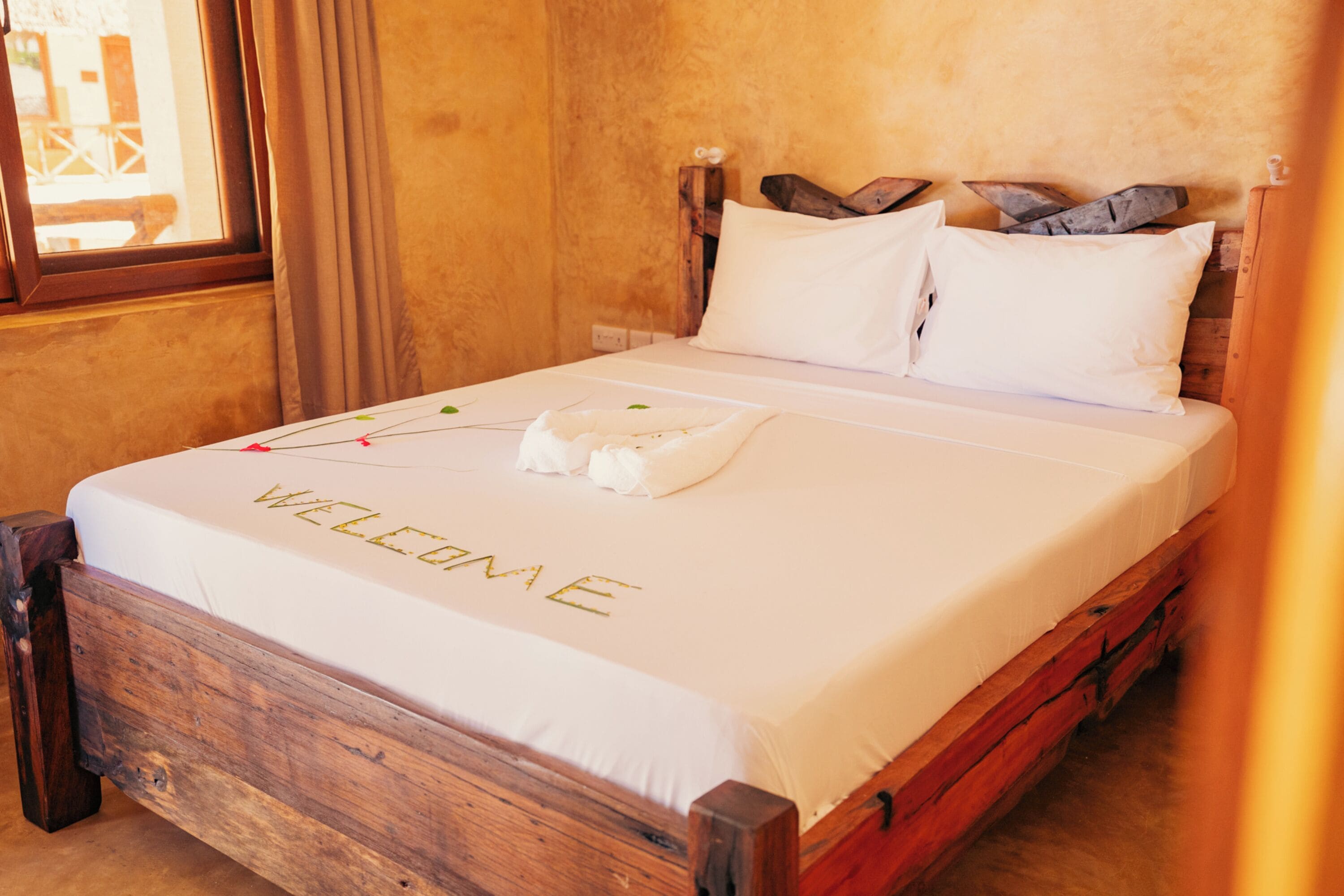 A bed with a white bedspread and a welcome mat.