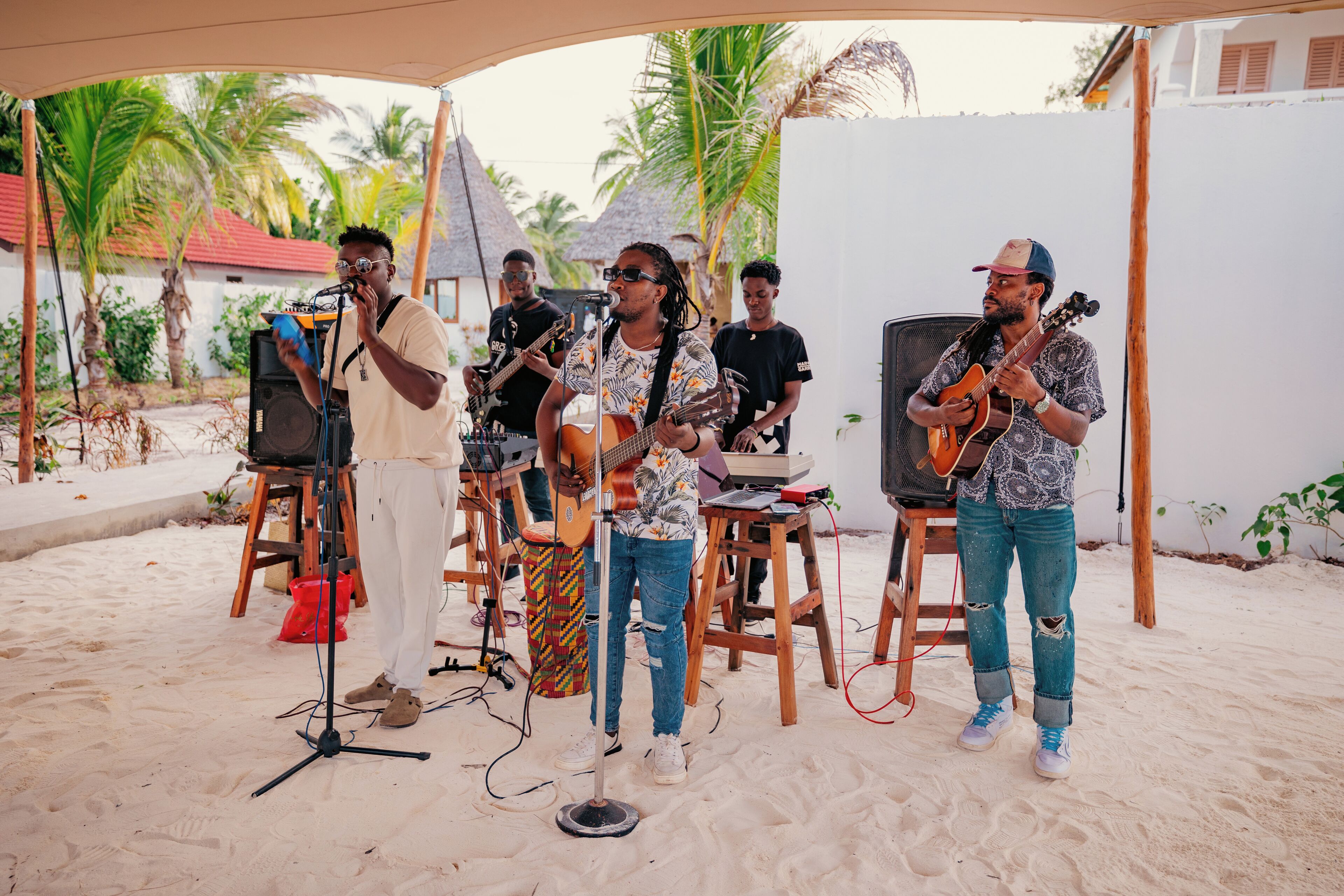 A group of musicians performing on a sandy stage with musical instruments and a microphone stand.