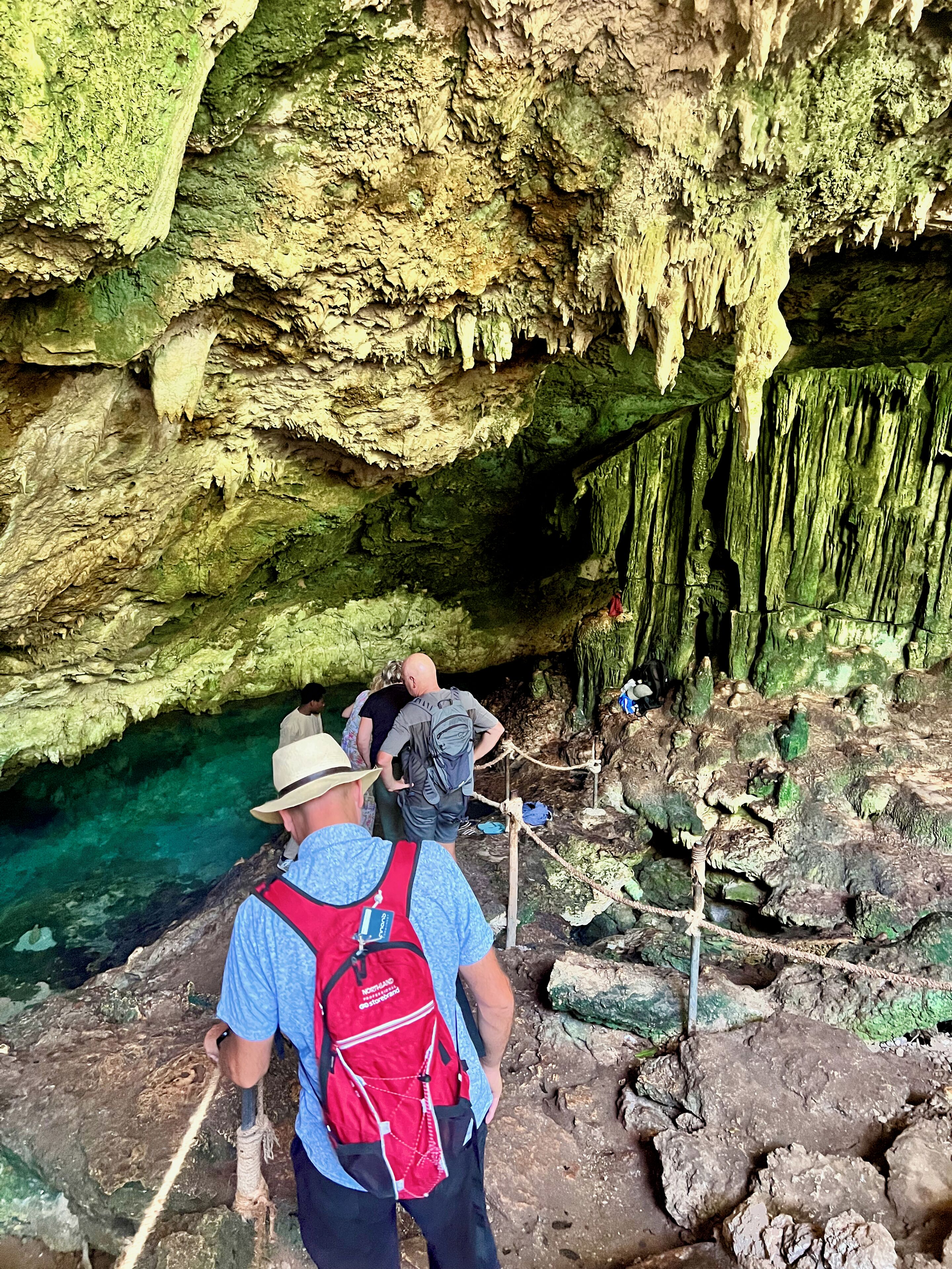 Eine Höhle mit Stalaktiten und Stalagmiten, einer Seilsperre und einer Person mit Rucksack.