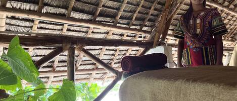 Una habitación con techo de paja, una planta grande y una cama.