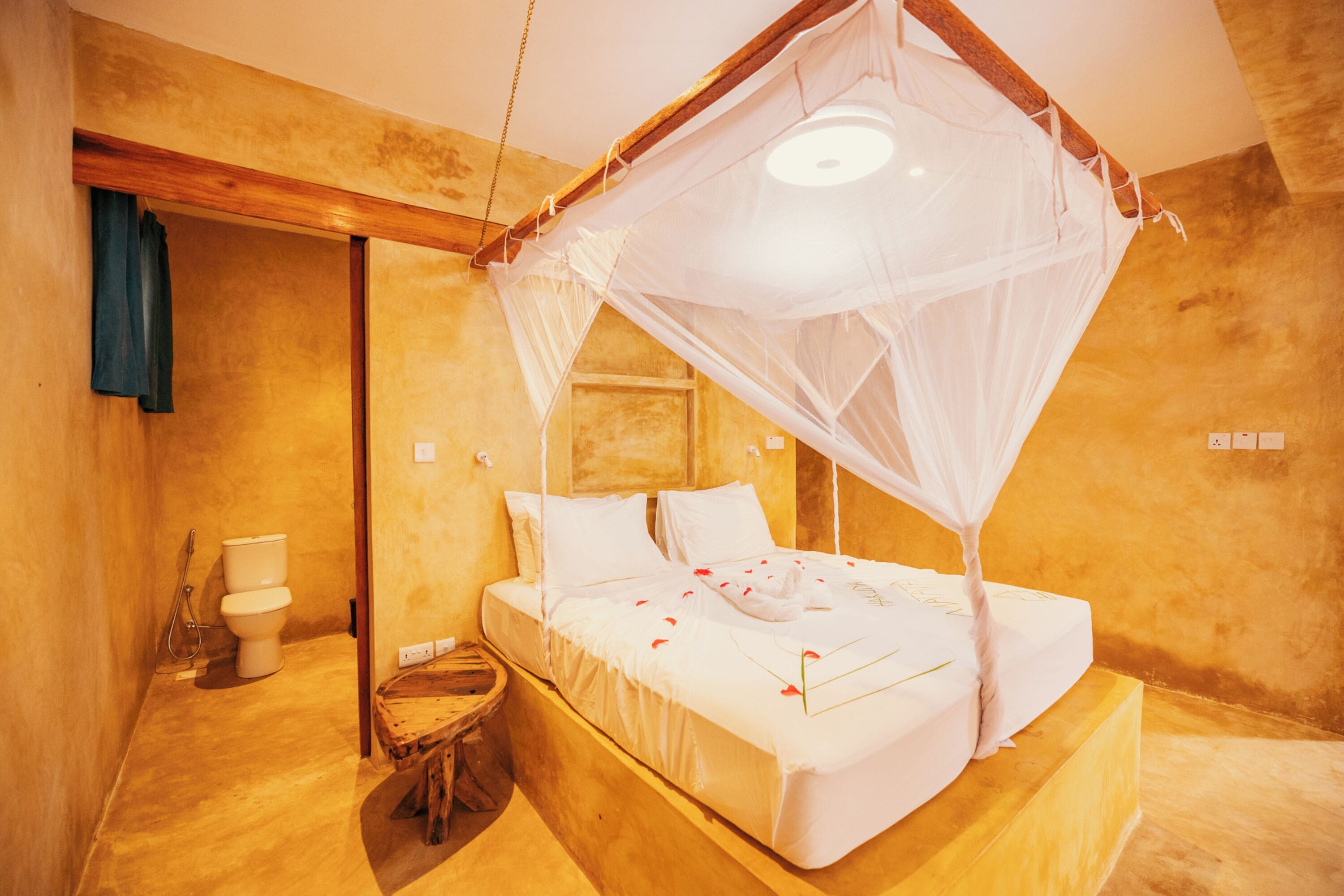 Una habitación con una cama bajo un dosel, un taburete de madera y un inodoro.