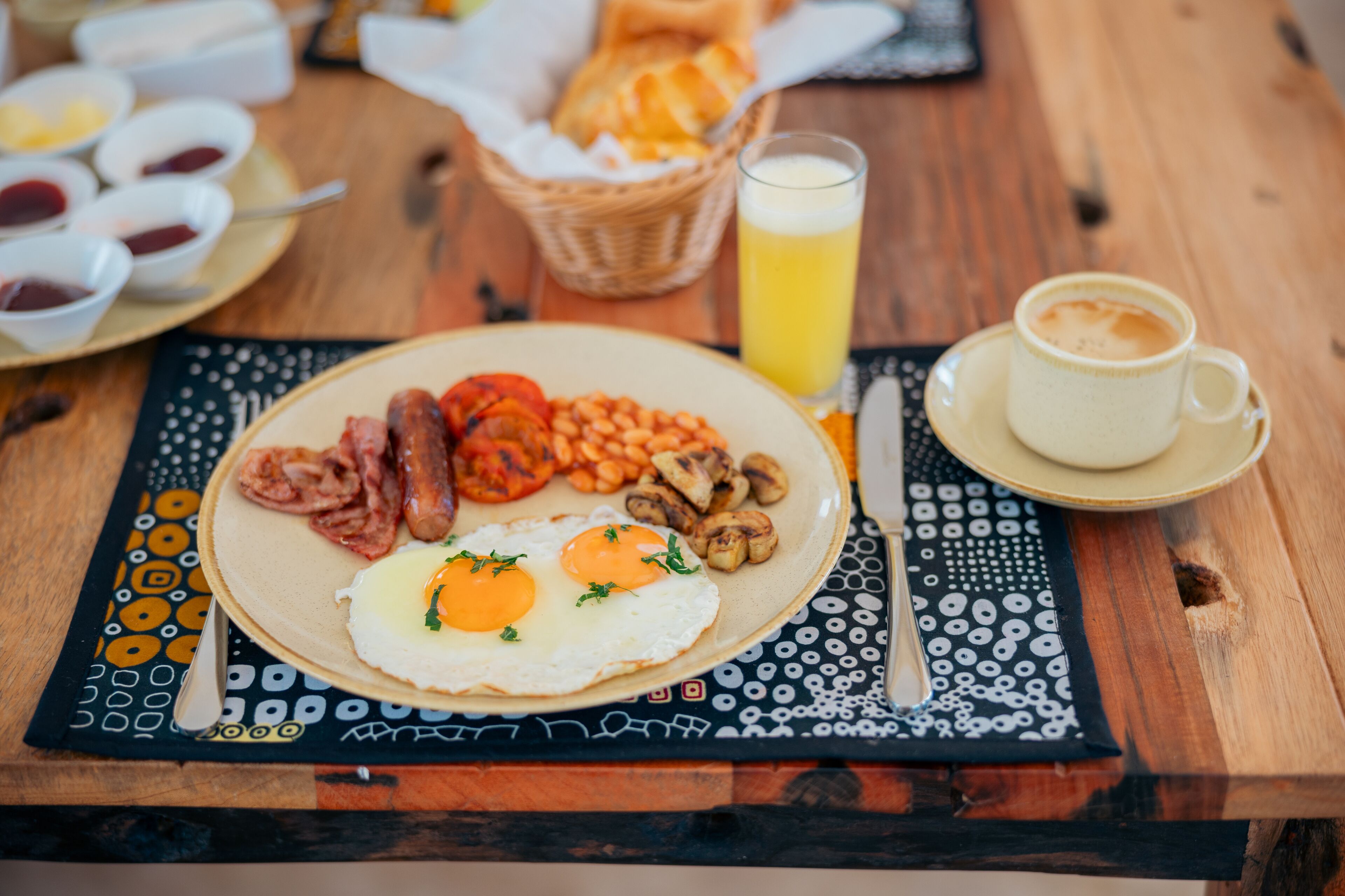 Un plato de desayuno con huevos, salchichas, frijoles y champiñones sobre un mantel individual estampado.