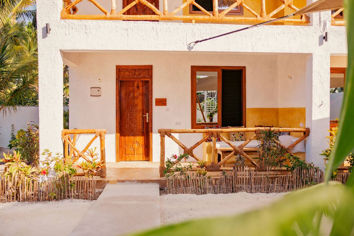 Un edificio blanco con puerta de madera, balcón y pequeño jardín con plantas.