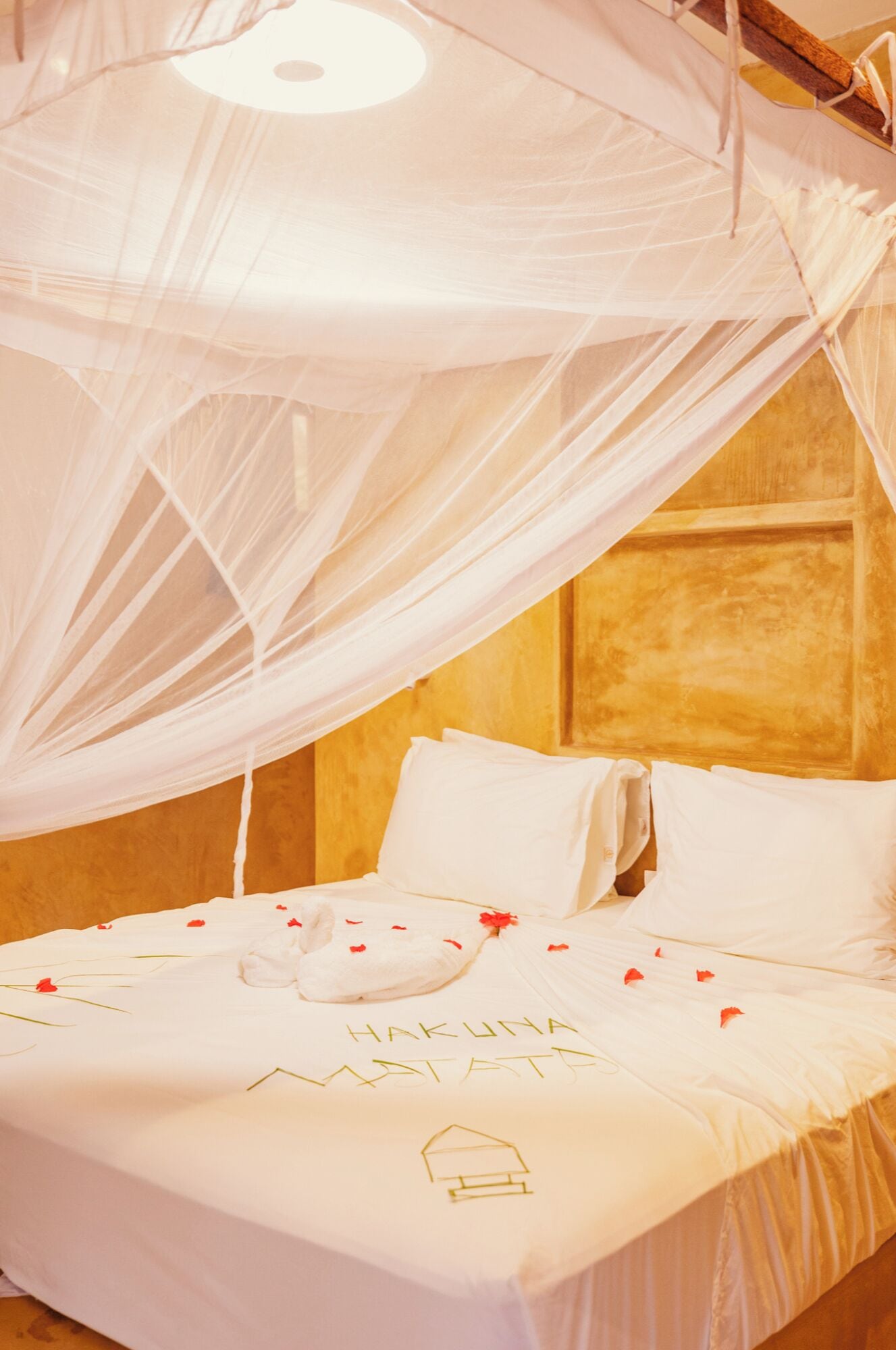 A bed with a canopy, white bedding, and a pillow with 'HAKUNA MATATA' embroidered on it.