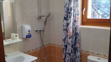 Ein Badezimmer mit Dusche, Toilette, Waschbecken und einem Fenster mit Blick auf Bäume.