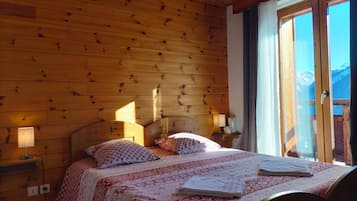 Une chambre aux murs lambrissés, avec un lit, des lampes de chevet et une fenêtre donnant sur les montagnes.